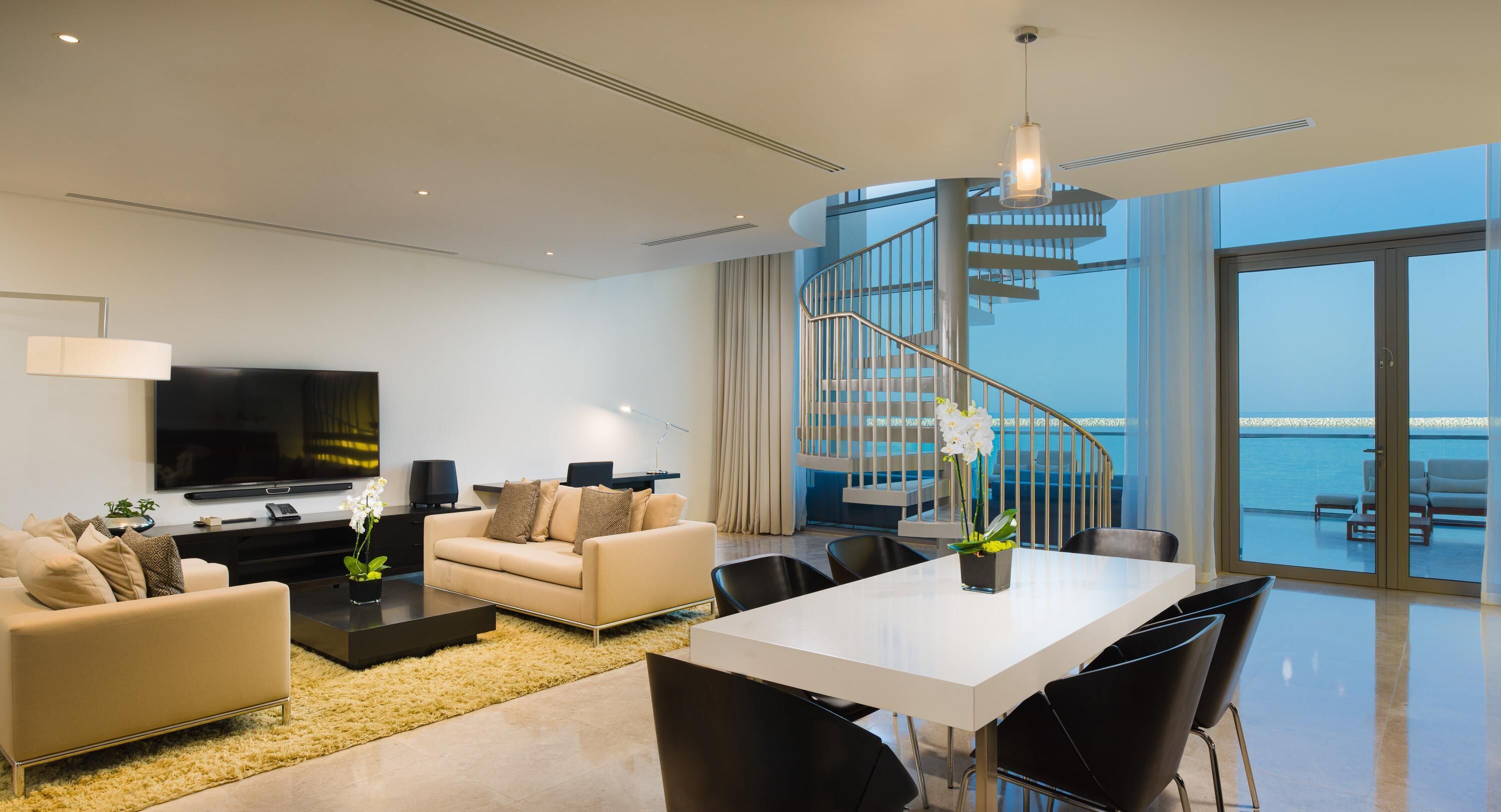 Un salon moderne comprenant un canapé, un téléviseur et un coin repas avec des chaises et une table.