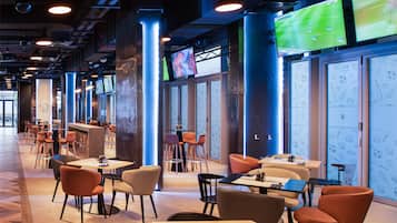 A modern indoor space with multiple seating areas, including tables and chairs, and large screens displaying sports events.