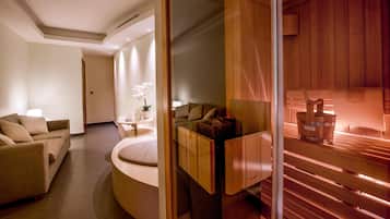 Ein moderner Spa-Raum mit einer Holzauna, einem Massagetisch und einer Sitzecke mit einer Couch und einem kleinen Tisch mit einem Blumenstrauß.