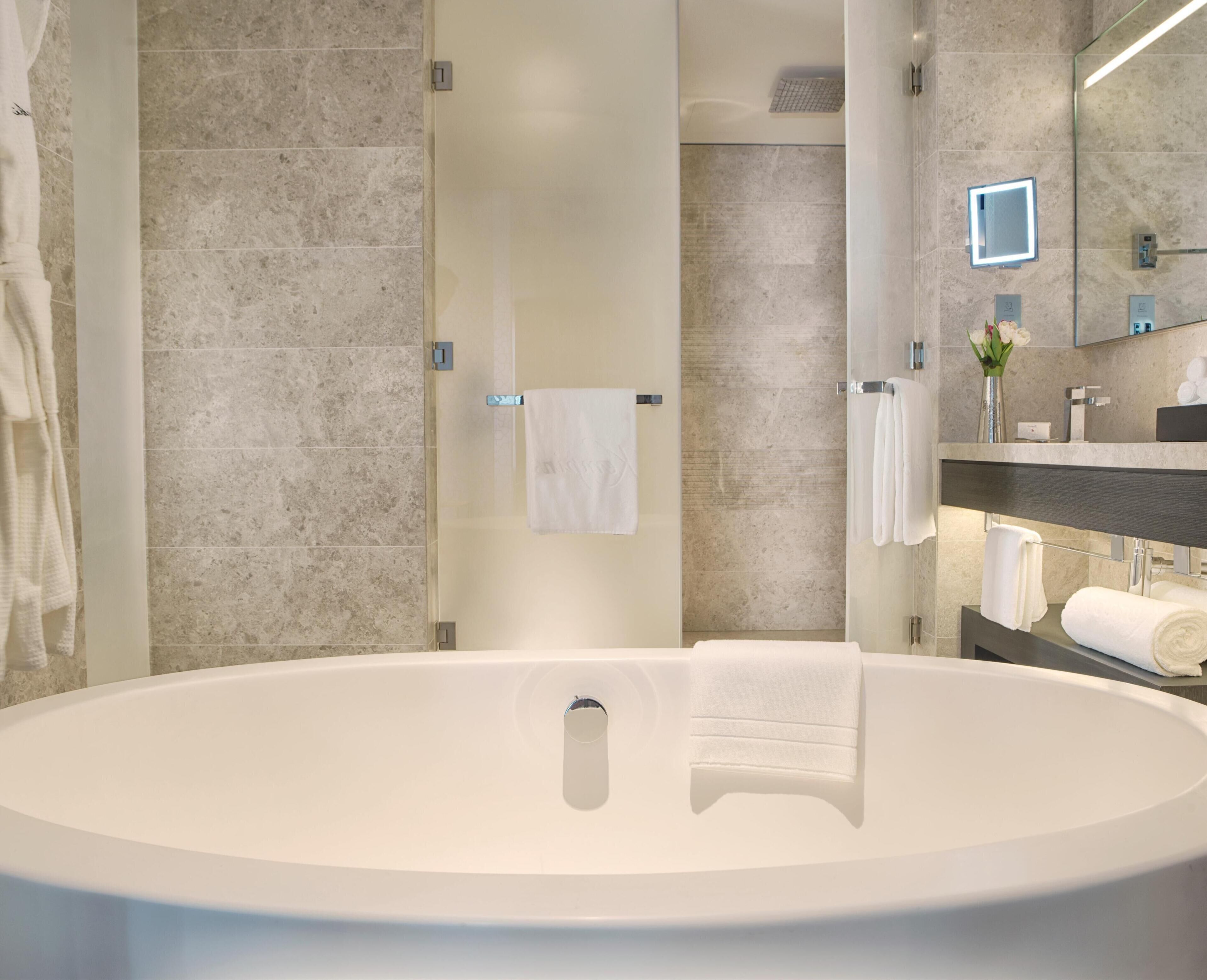 A modern bathroom with a large bathtub, a glass shower enclosure, and a vanity with a mirror and towel rack.