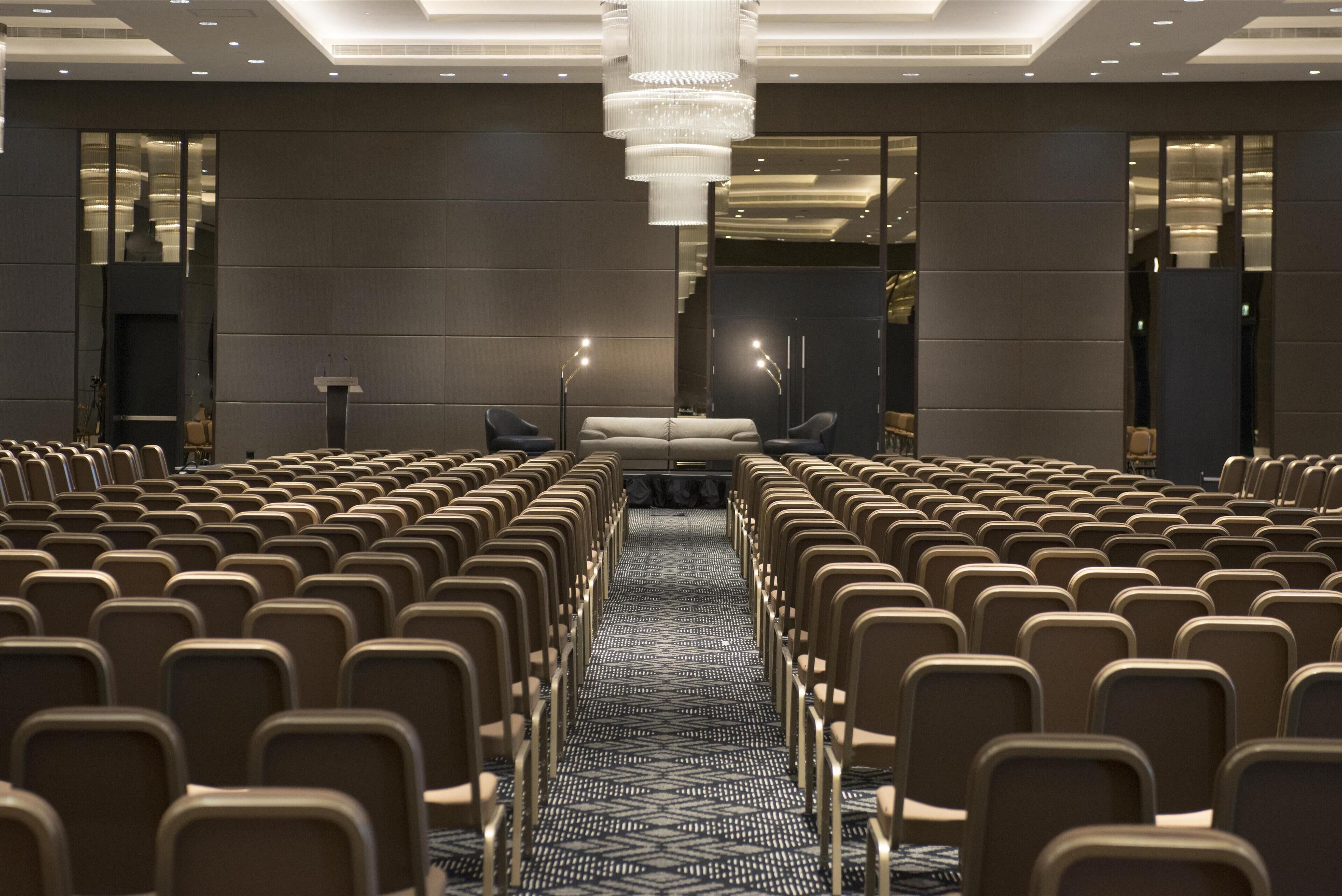 A conference room with rows of chairs, a podium, and a chandelier.