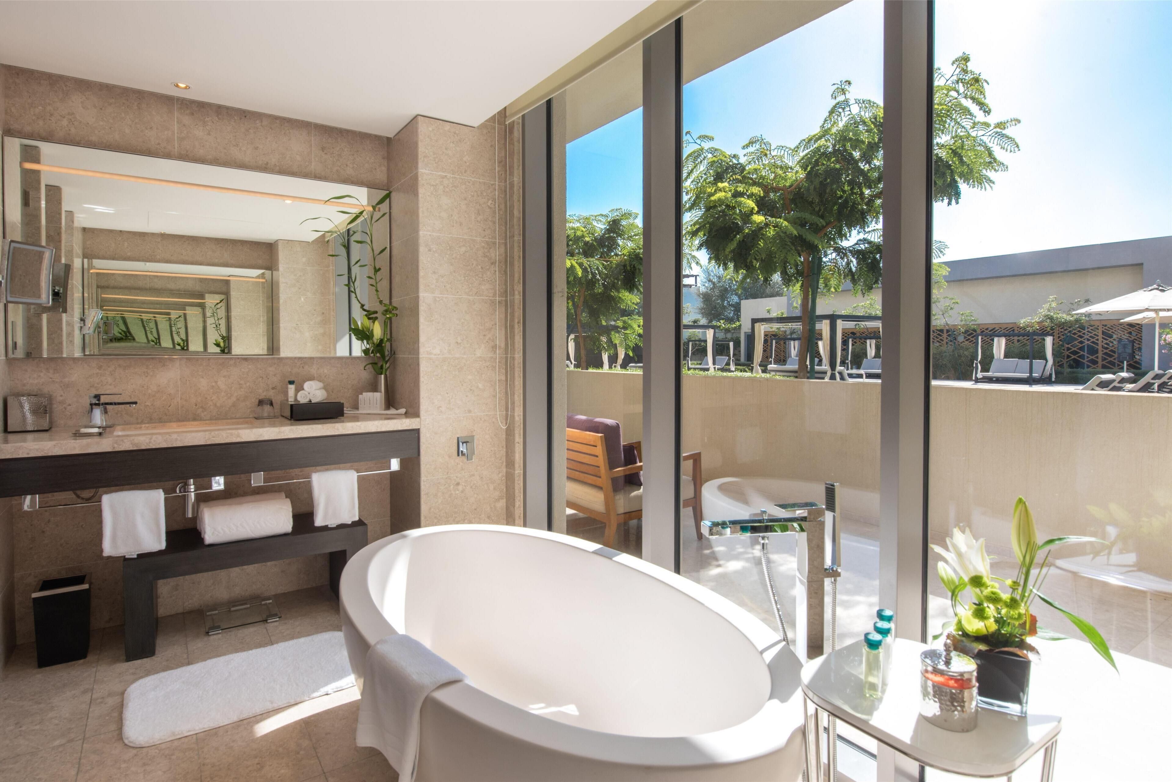 A modern bathroom with a large bathtub, a vanity with a mirror, and a view of the outdoor area.