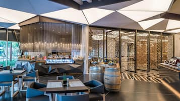 Un restaurant moderne doté d’un plafond au design géométrique, d’un bar où sont exposées des bouteilles et d’un espace détente avec des tables et des chaises.