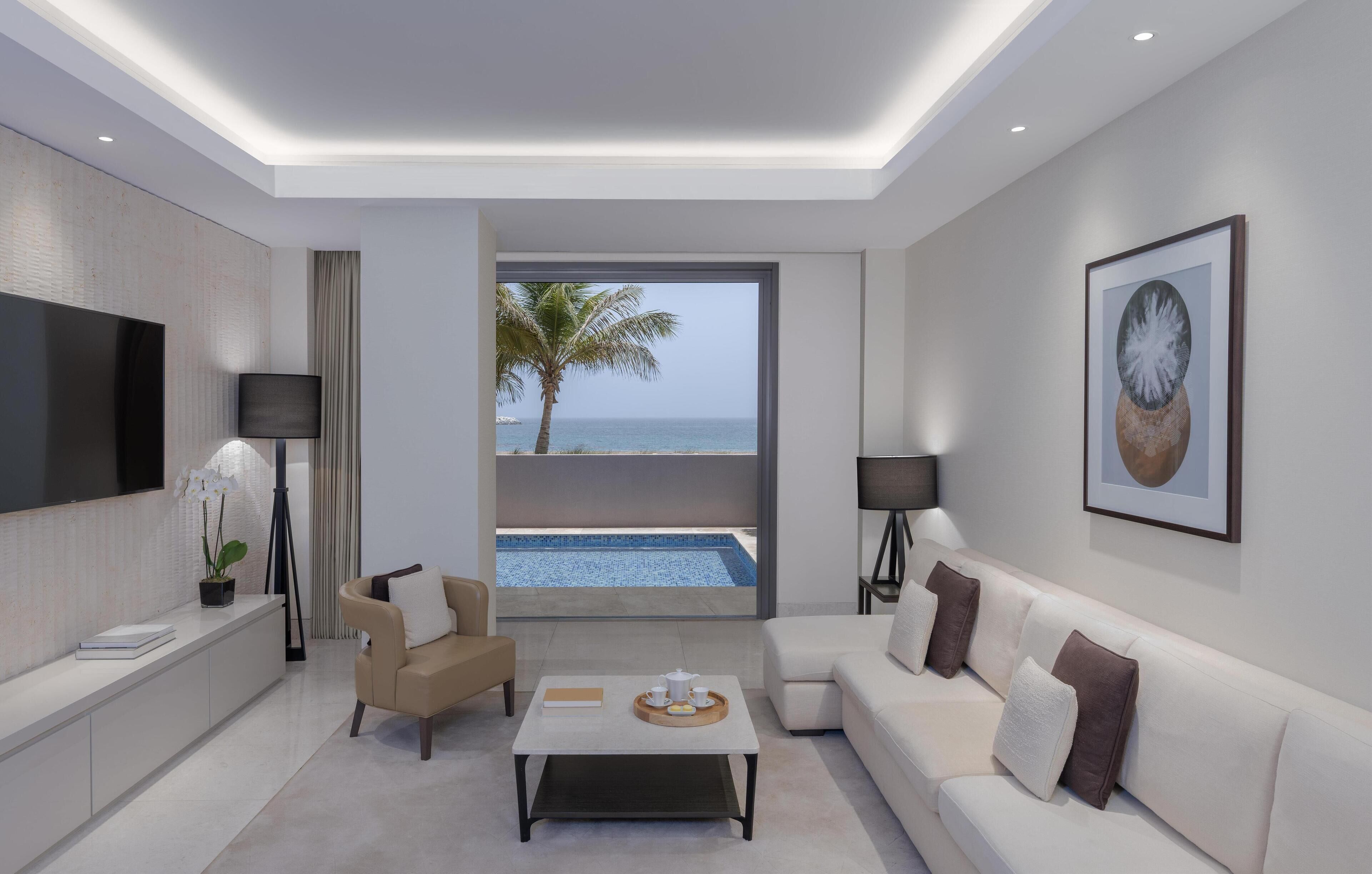 A modern living room with a large TV, a sofa, a coffee table, and a view of the ocean.