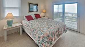 A bedroom with a bed, a nightstand, a lamp, a framed picture, and a view of a balcony. - Bright's Beach Front | Sound View + Walk to Beach! (Topsail Beach)