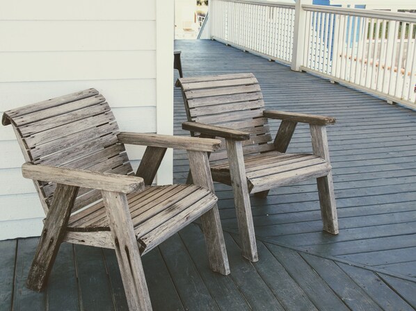 Two wooden chairs on a wooden deck with a white railing in the background.