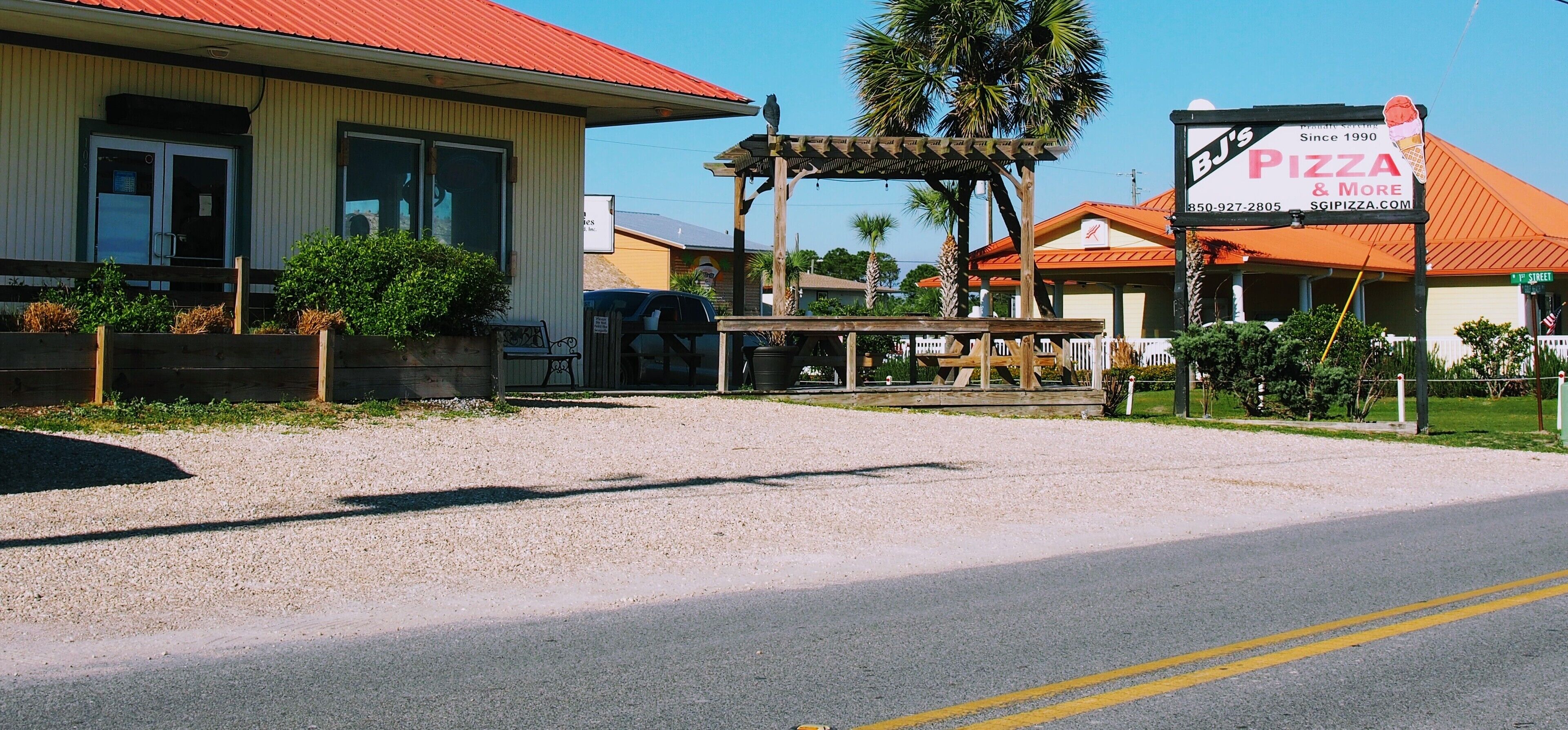 A building with a red roof, a covered outdoor seating area, and a sign for BJ's Pizza & More.