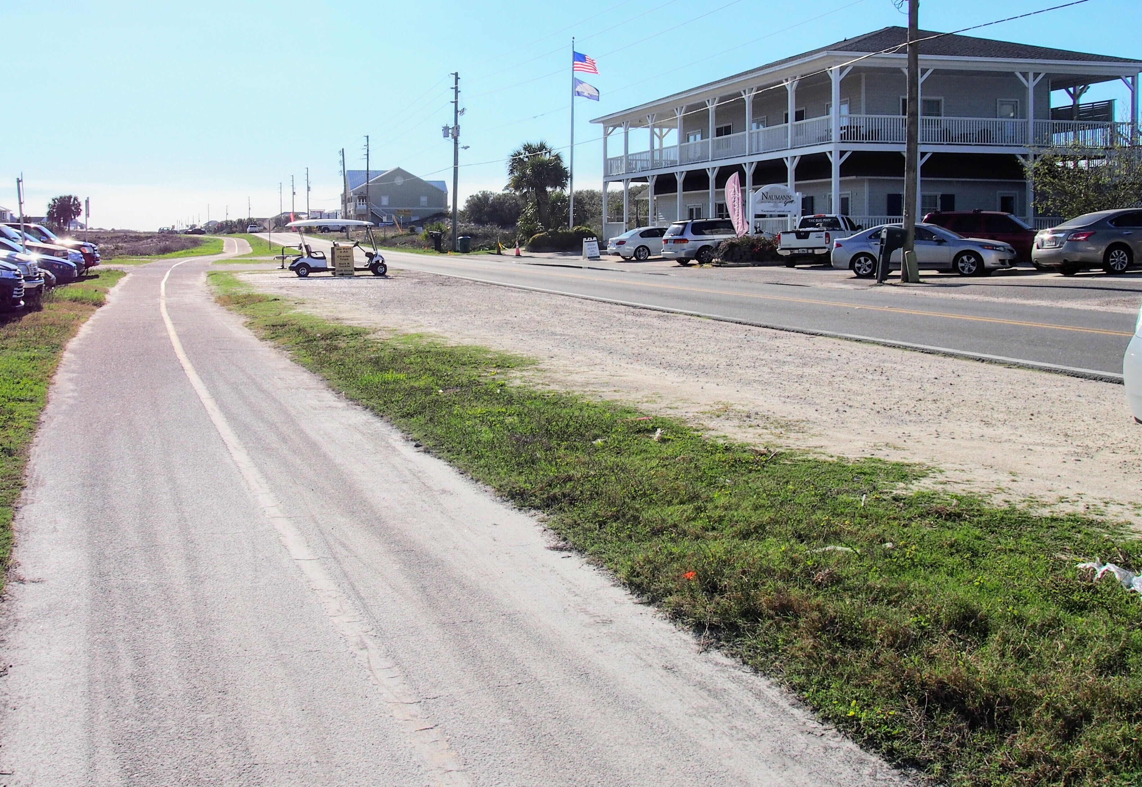 A coastal road with a building featuring a balcony and a flag.
