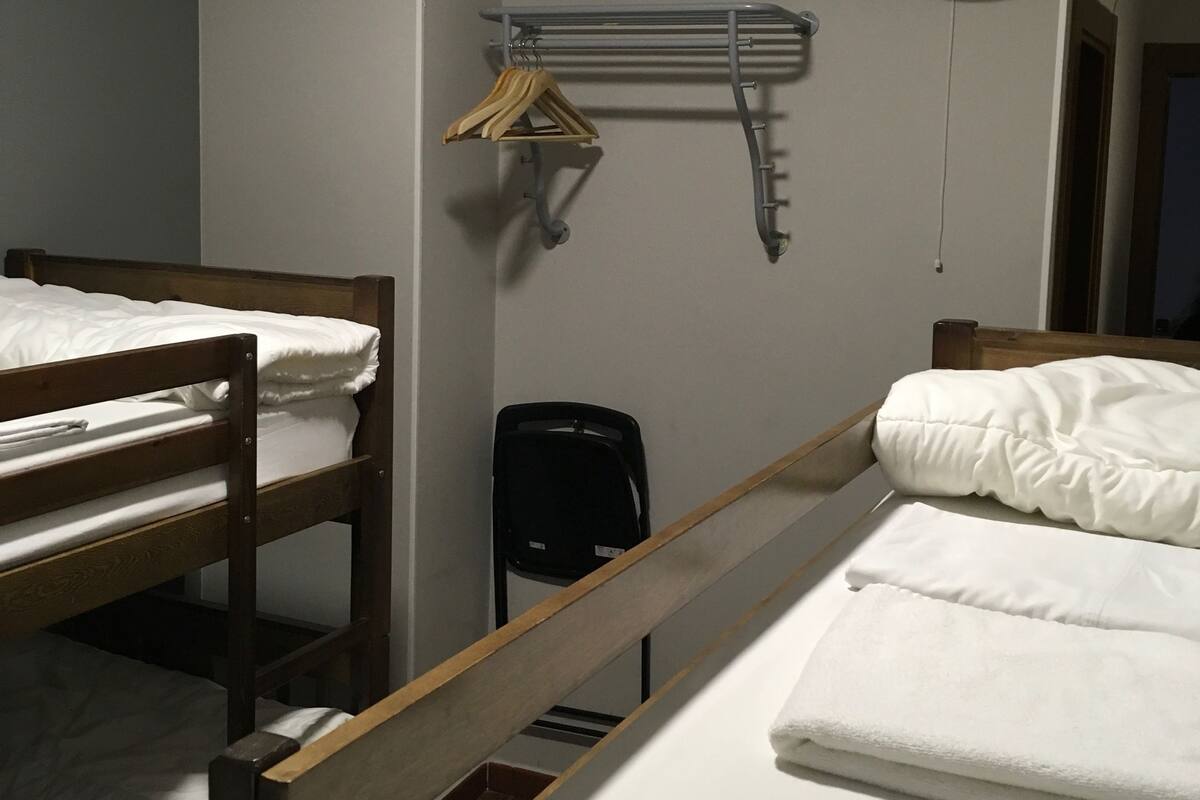 A dormitory room with two bunk beds, a wall-mounted fan, and a drying rack with clothes.