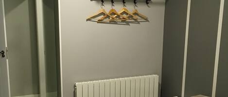 A bedroom with a bed, a radiator, a wall-mounted drying rack, and a door leading to another room.