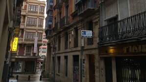 A narrow street with multi-story buildings, some with balconies and signage indicating businesses. - Pensión La Bilbaina - Albergue Logroño (Logroño)