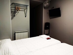 A hotel room with a bed, a radiator, a wall-mounted TV, a fan, and a towel rack. - Pensión La Bilbaina - Albergue Logroño (Logroño)