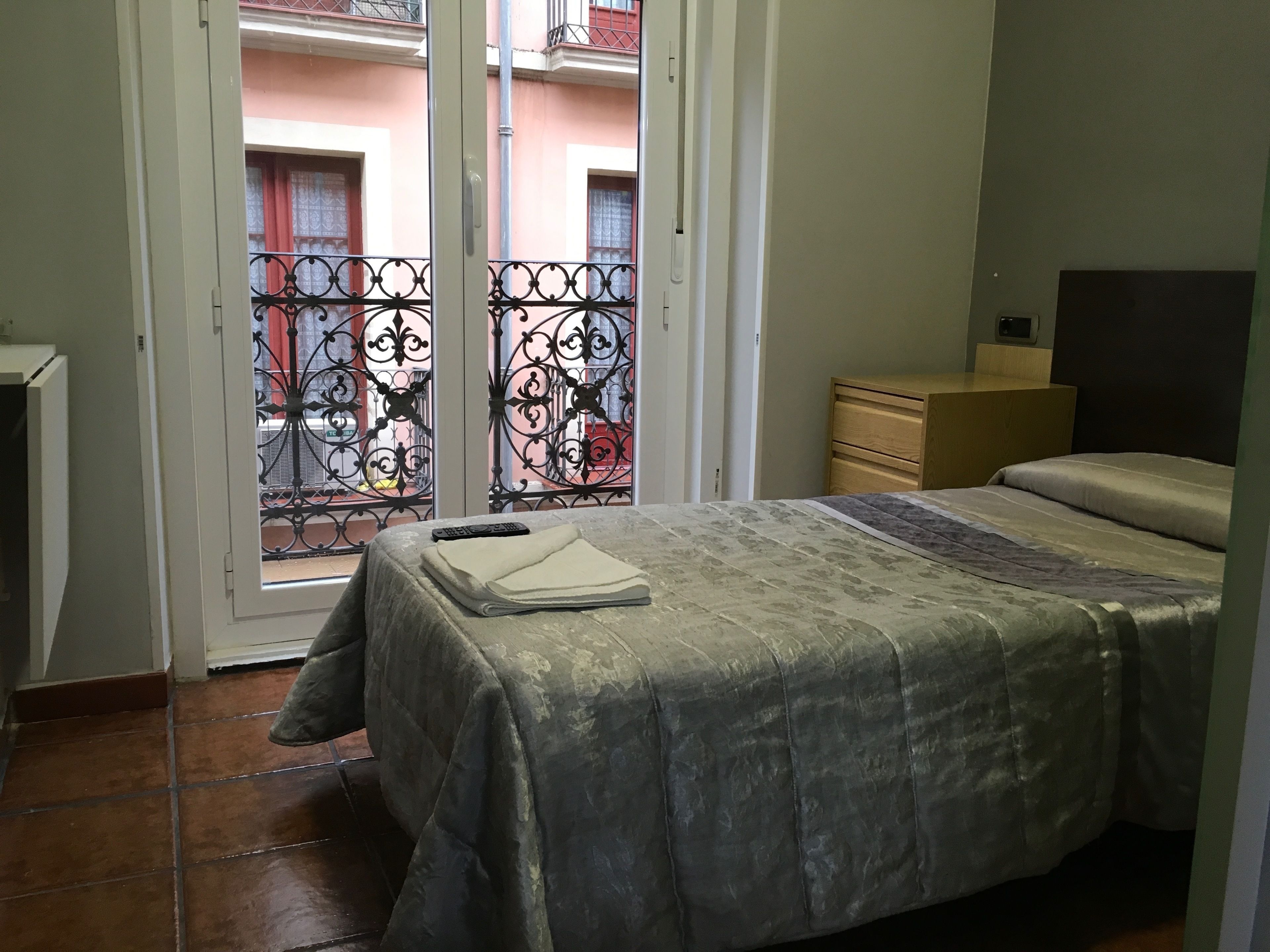 Een slaapkamer met een bed, een houten nachtkastje, een dressoir en een schuifdeur naar een balkon.