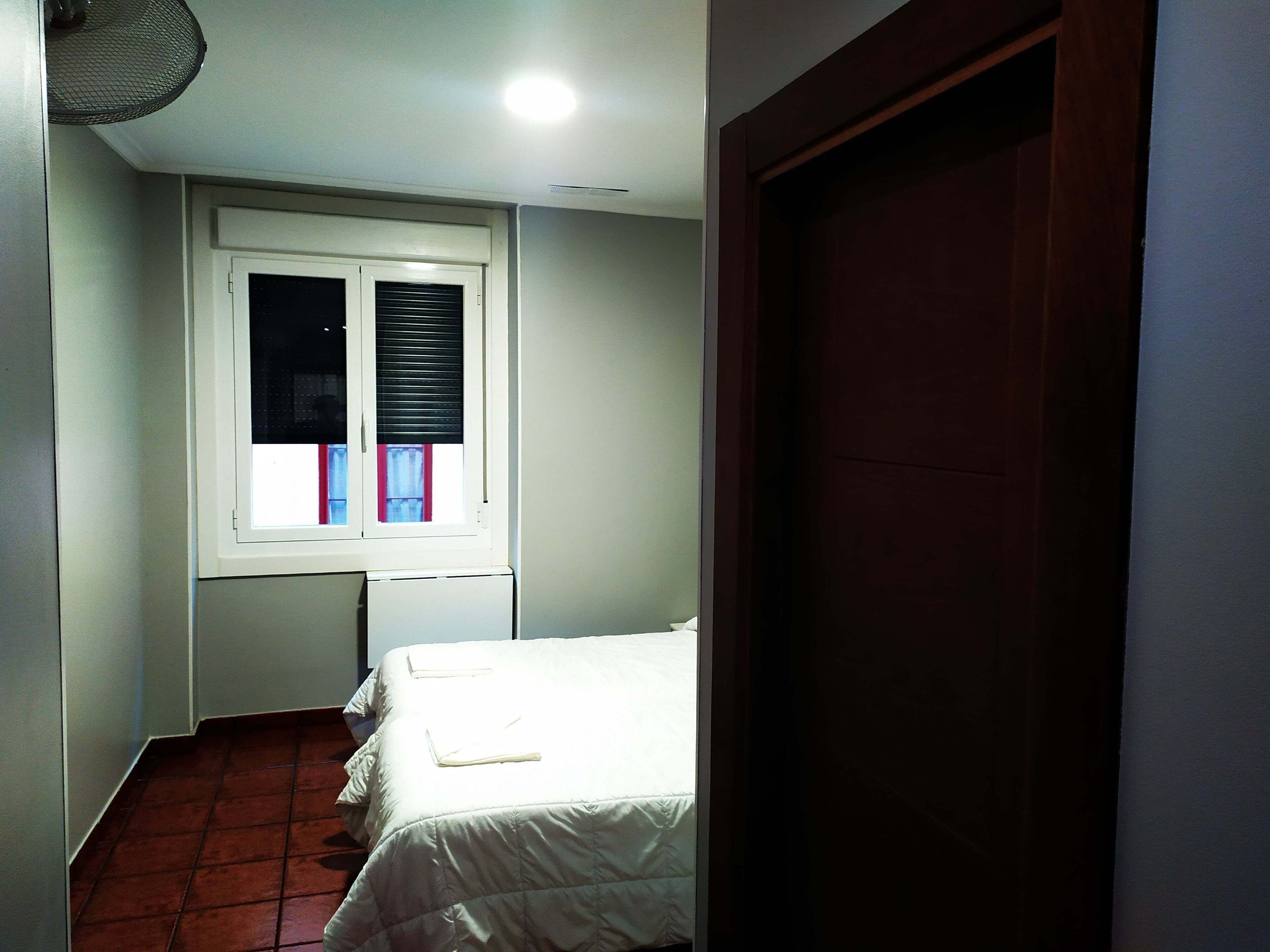 Un dormitorio pequeño con una cama individual, una ventana con persianas y una puerta.