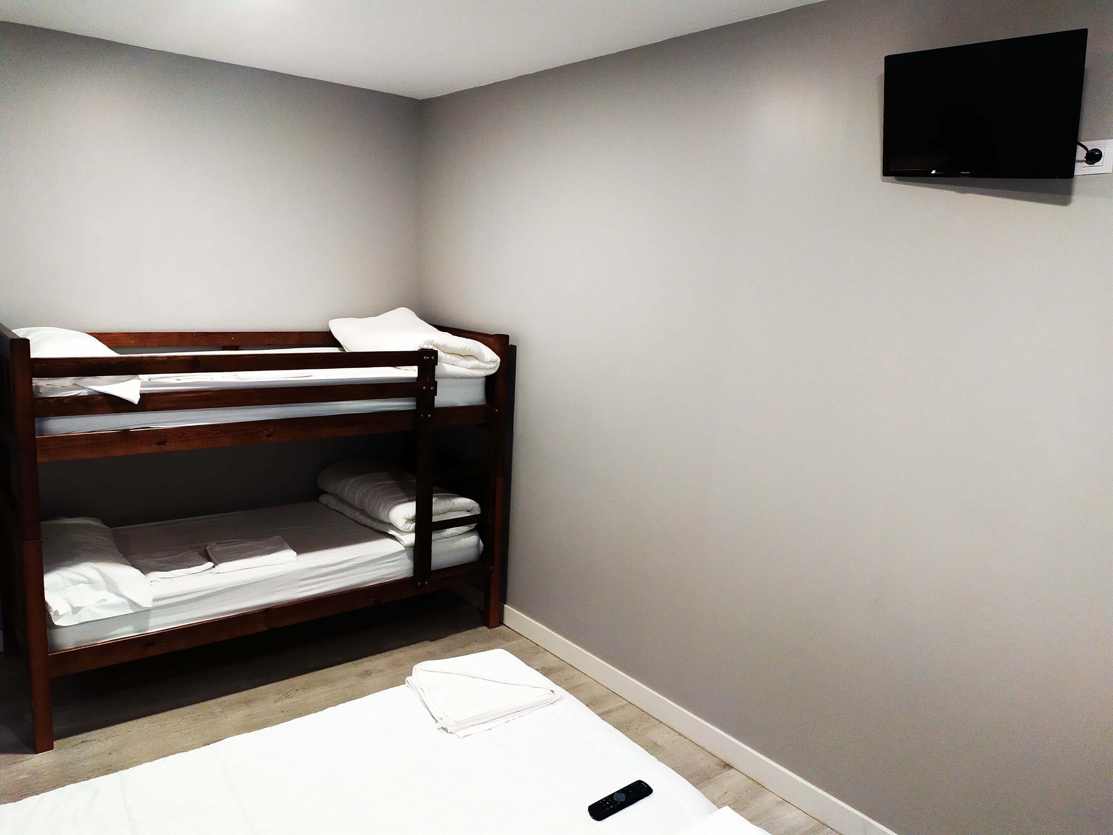 Un lit superposé avec une literie blanche, dans une chambre où un téléviseur à écran plat est fixé au mur.