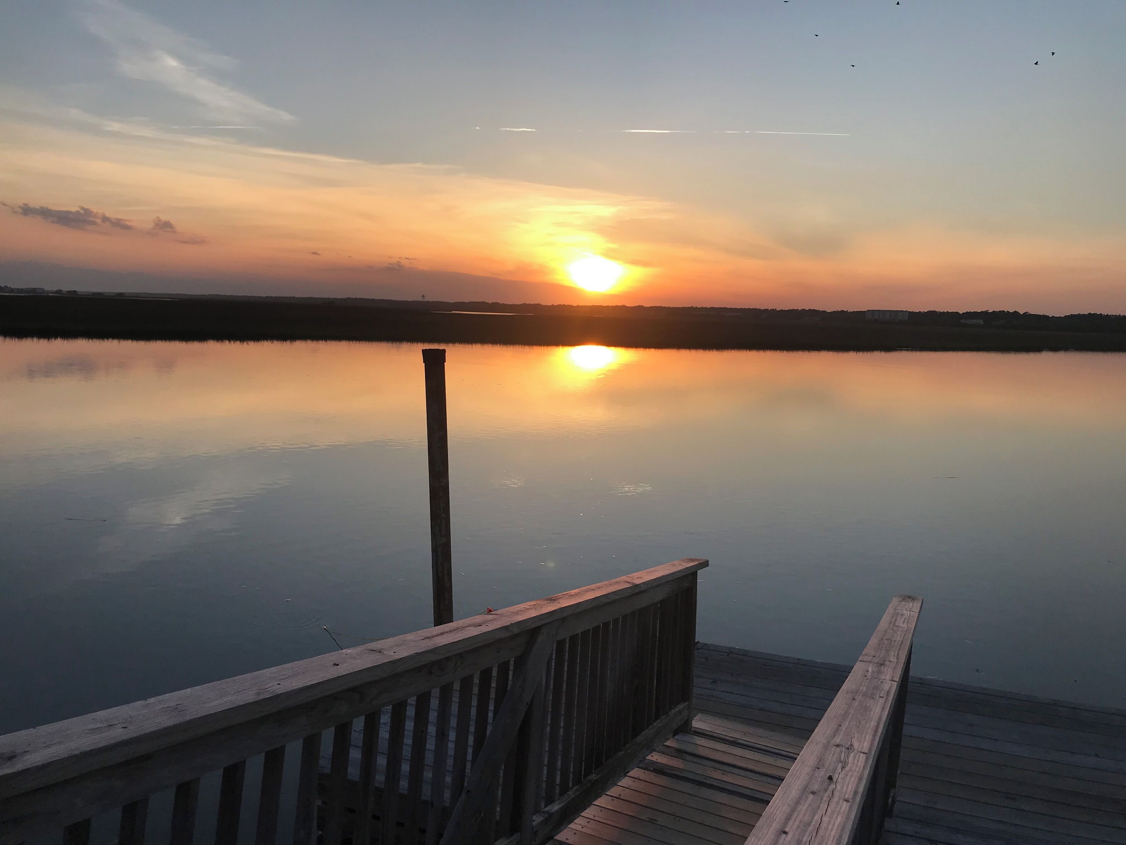 A wooden dock extending into calm water with a sunset in the background.