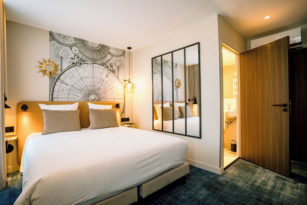 Une chambre d’hôtel avec un grand lit, une carte géographique accrochée au mur, un miroir et une porte en bois.