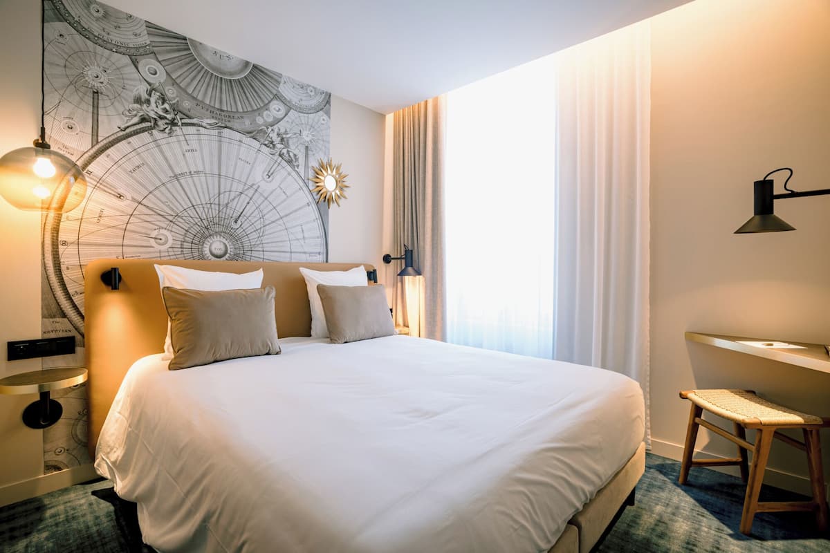 Une chambre d’hôtel avec un grand lit, un bureau, une chaise et un globe terrestre fixé au mur.
