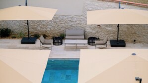 Un área de piscina con dos sombrillas color beige, un sofá y dos sillones.