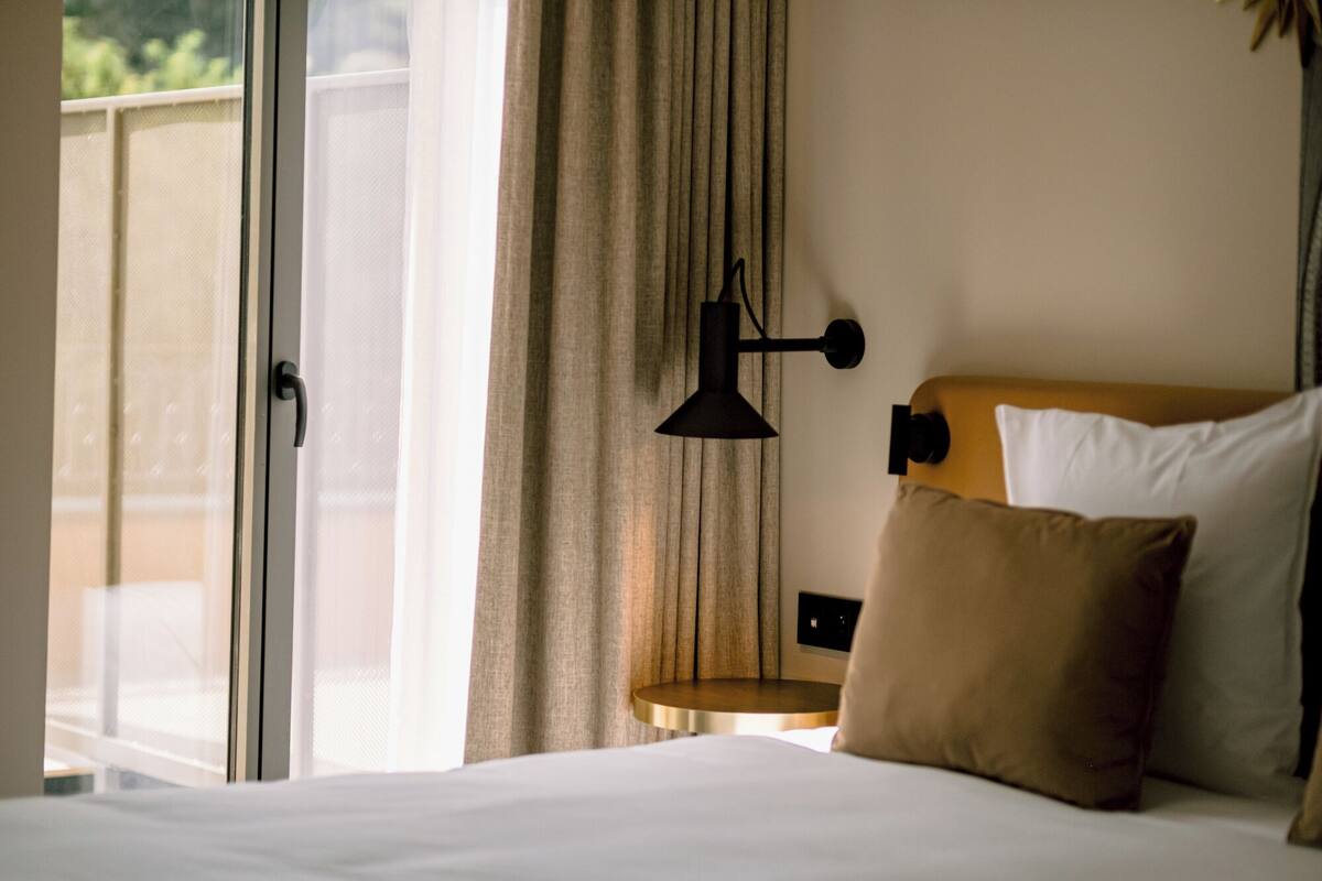 Une chambre d’hôtel avec un lit, une table de chevet, une lampe et une vue sur l’extérieur.