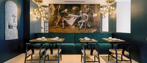 Un comedor moderno con un mural grande, dos mesas con sillas y un sofá verde.