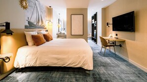 A hotel room with a large bed, a desk with a chair, a flat-screen TV, and a painting on the wall.
