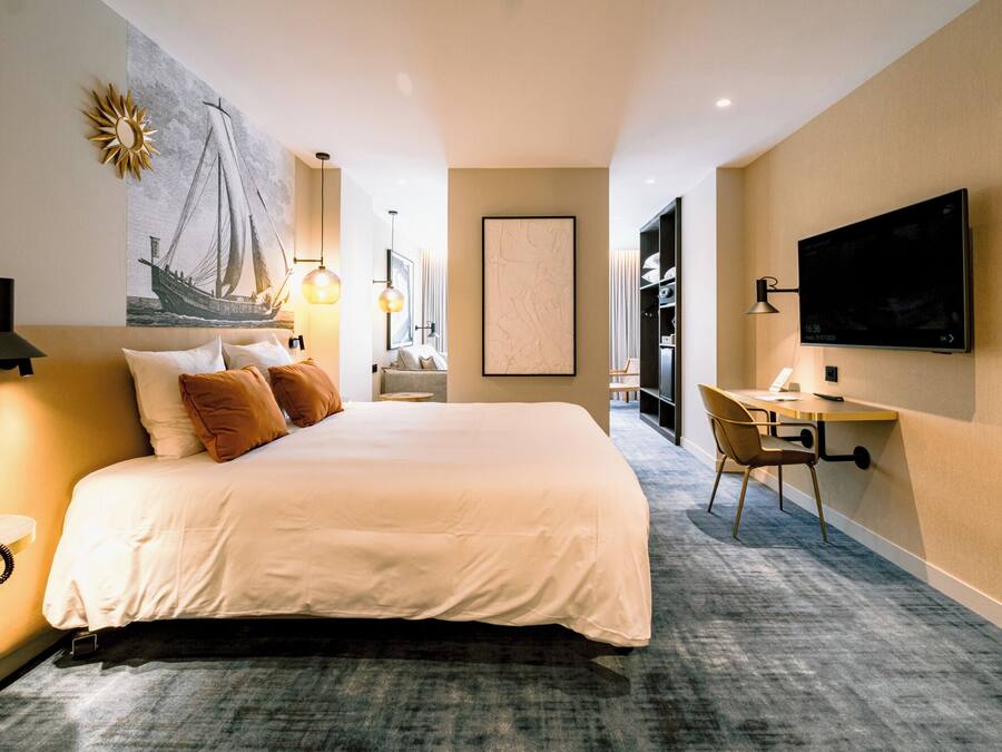 Ein Hotelzimmer mit einem großen Bett, einem Schreibtisch mit Stuhl, einem Flachbildfernseher und einem Bild an der Wand.