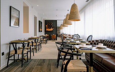 A modern dining area with multiple tables and chairs, a leather booth, and hanging wicker lamps.