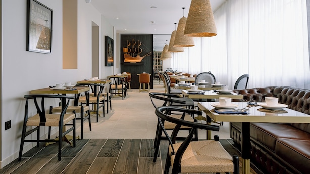 Un comedor moderno con varias mesas y sillas, un banco de cuero y lámparas de mimbre colgantes.