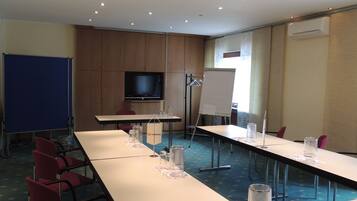 A conference room with long tables, red chairs, a whiteboard, a screen, and an air conditioning unit.