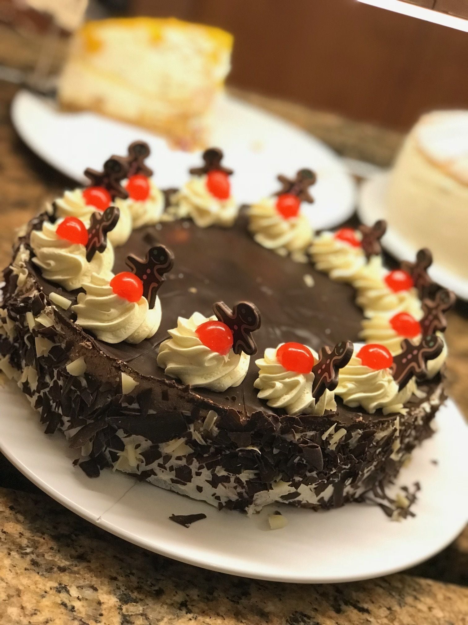 Un pastel de chocolate con crema batida y cerezas sobre un plato blanco.