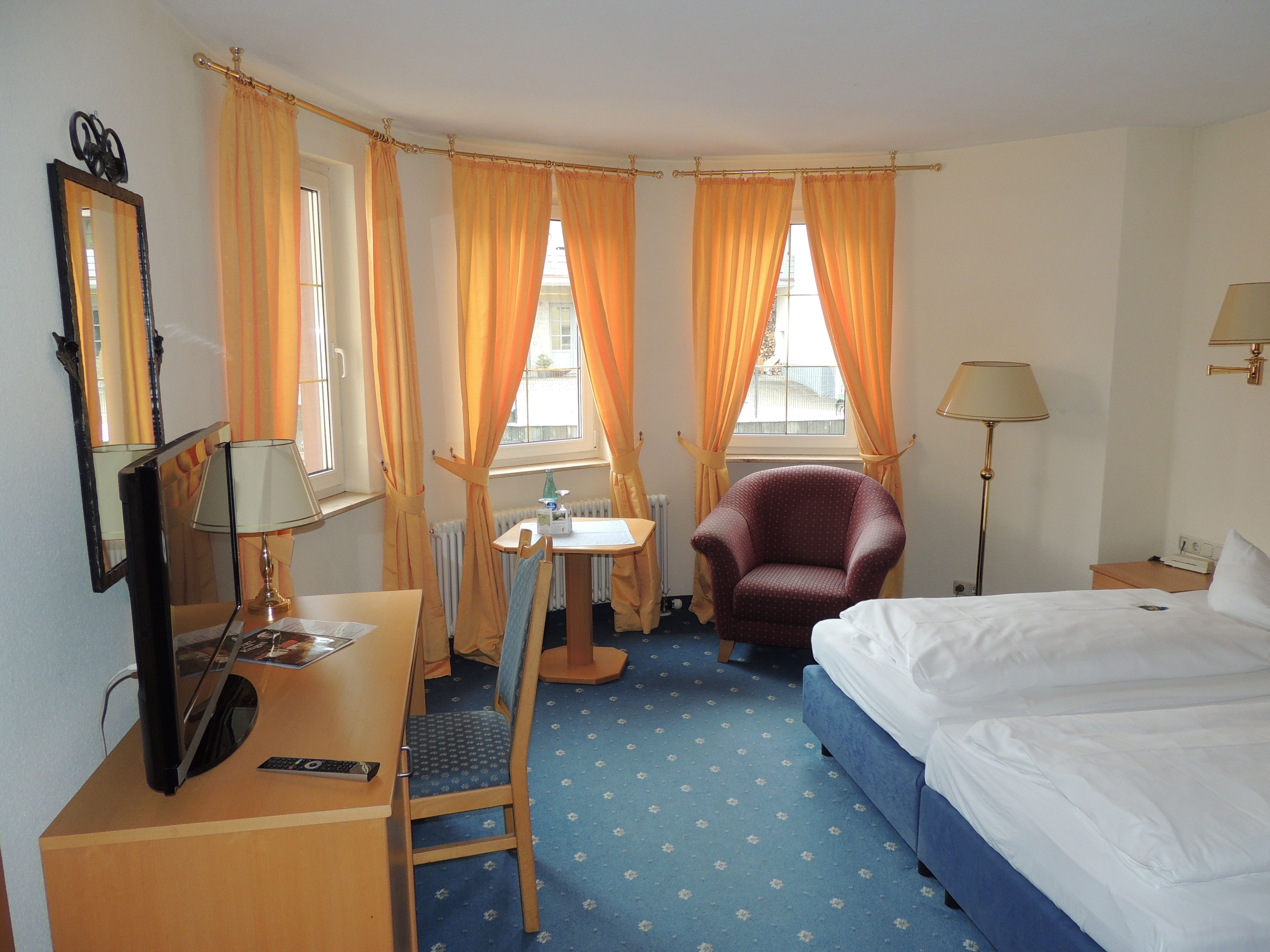 Una camera d'albergo con un letto, una scrivania con un computer, una sedia, una lampada e una finestra con tende.