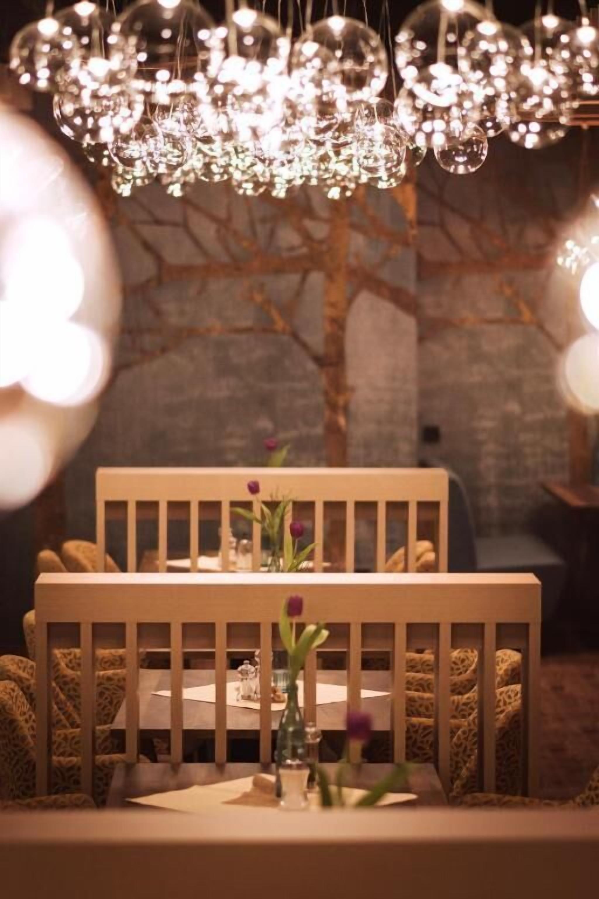A dining area with a table set for two, a chandelier overhead, and a tree in the background.