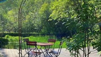 An outdoor wooden deck with a table and chairs, surrounded by lush greenery and trees.