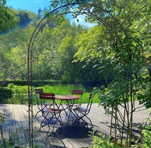 An outdoor wooden deck with a table and chairs, surrounded by lush greenery and trees. - Hotel zum Engel (Mespelbrunn)