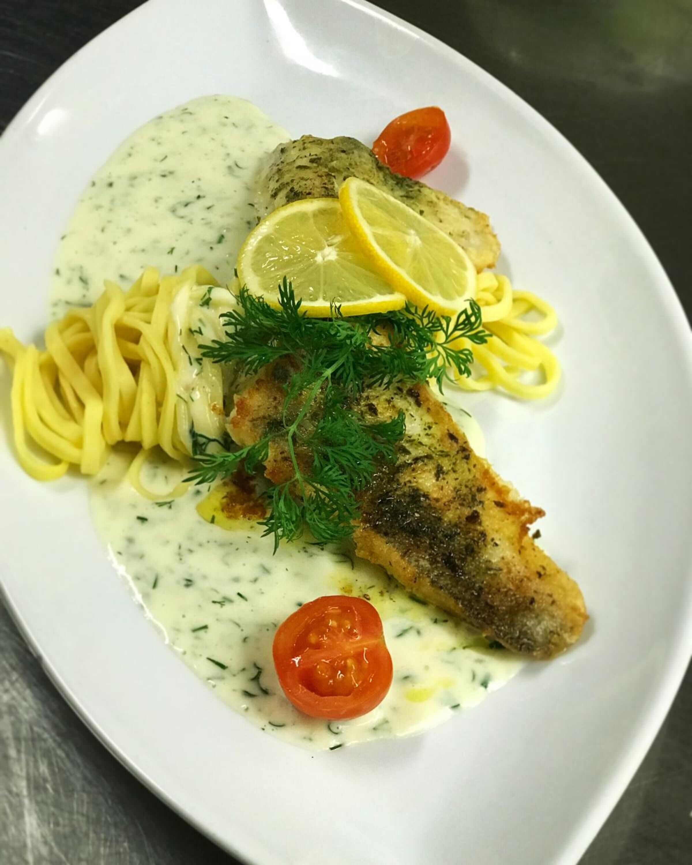 A plate with fish fillet, lemon slices, dill, and cherry tomatoes.