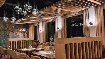 A restaurant interior with wooden slatted partitions, round hanging light fixtures, and patterned upholstered chairs.