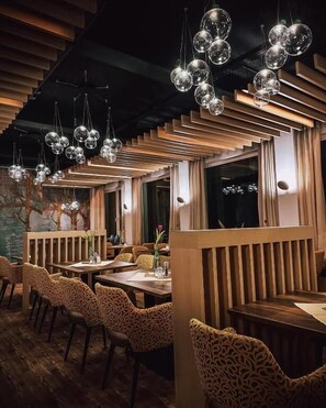 A restaurant interior with wooden slatted partitions, round hanging light fixtures, and patterned upholstered chairs. - Hotel zum Engel (Mespelbrunn)