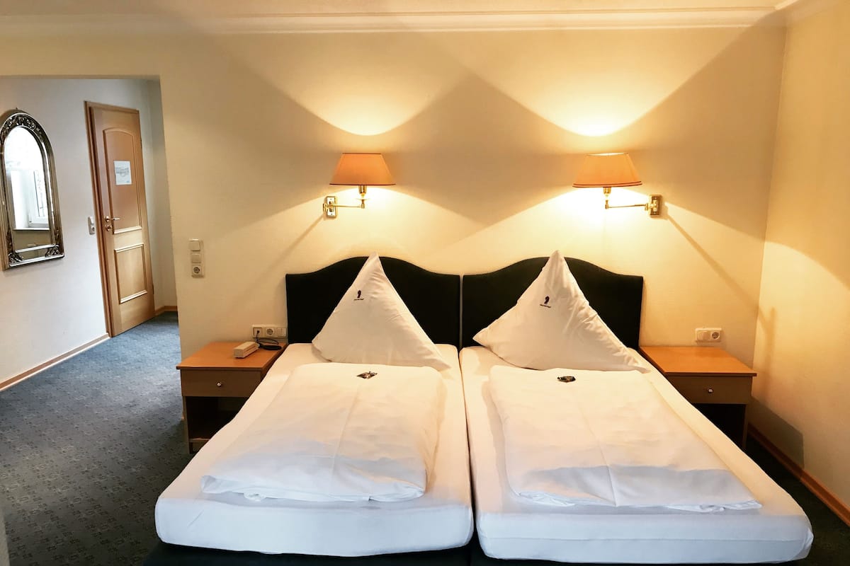 A hotel room with two single beds, a nightstand with a lamp, a mirror, and a door.