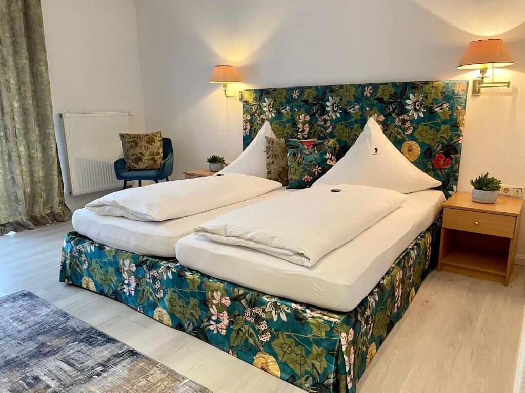 Ein Doppelbett mit Blumenmuster am Kopfteil, zwei Nachttischlampen, ein kleiner Nachttisch und ein Sessel.