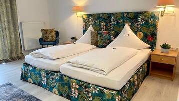 Una cama doble con cabecera floral, dos lámparas de noche, una mesita auxiliar pequeña y una silla.