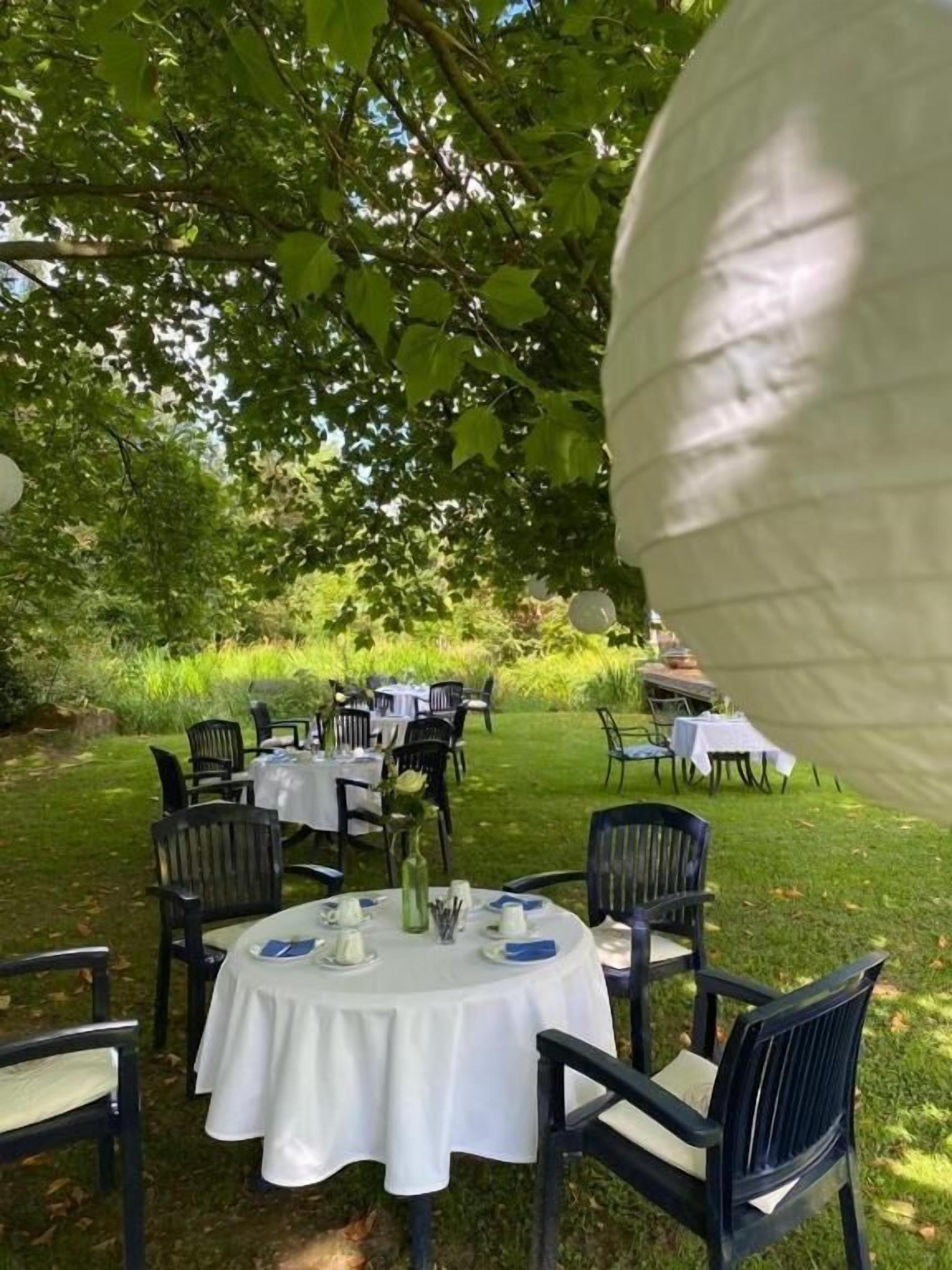 An outdoor dining area with round tables and chairs, surrounded by greenery.