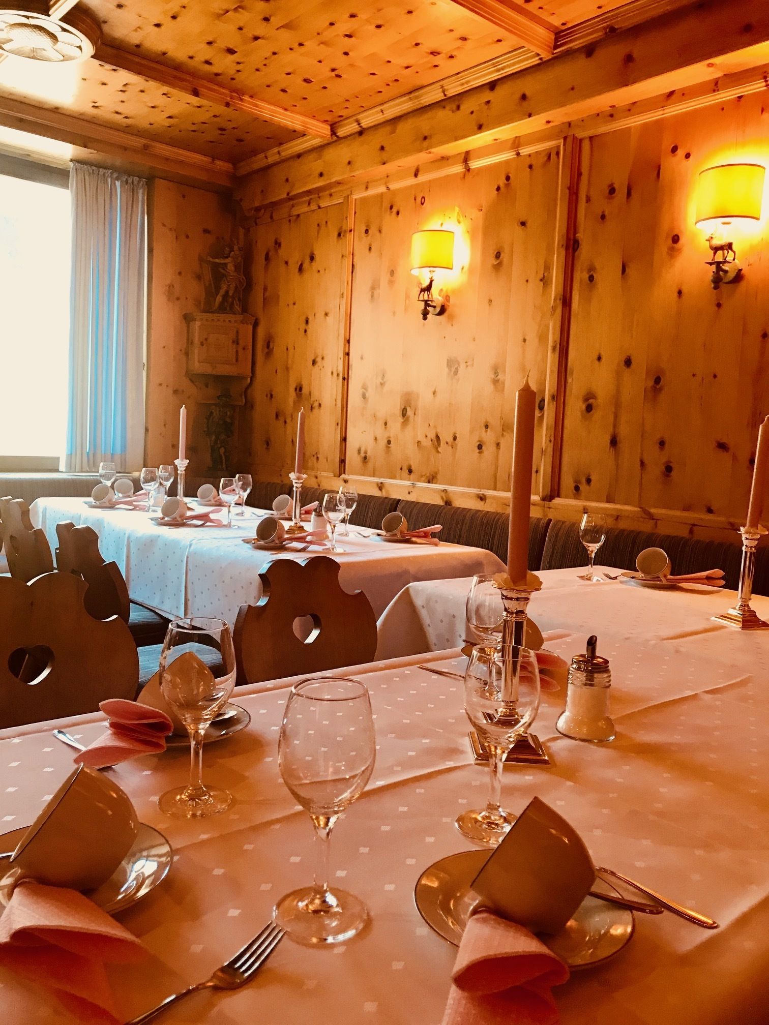 Un comedor con paredes de madera, mesas dispuestas con manteles blancos, velas y copas de vino.