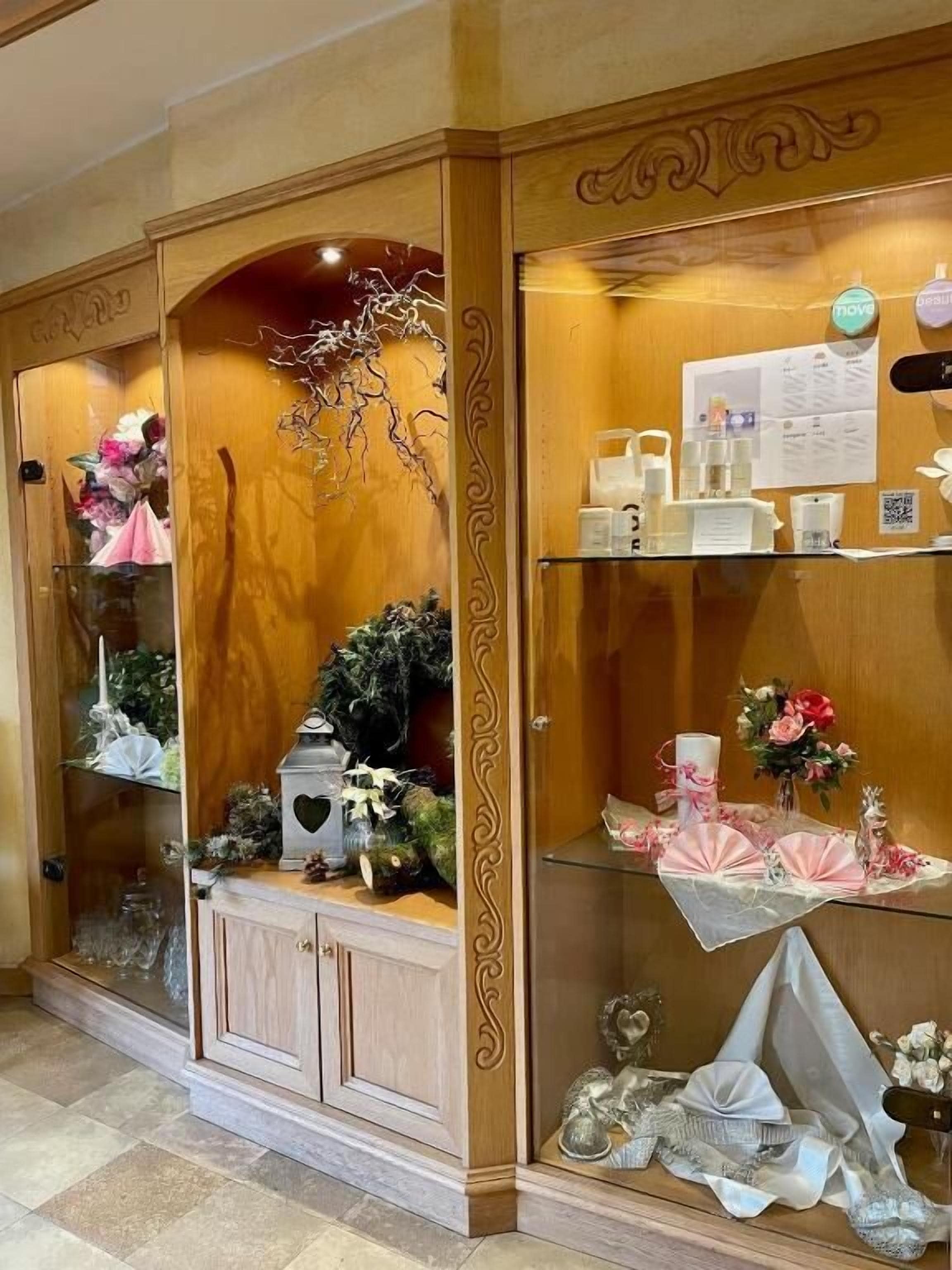 Un aparador de madera con puertas de cristal, que contiene diversos objetos como flores, velas y adornos decorativos.