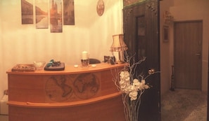 A reception desk with a world map design, a lamp, a vase with flowers, and framed pictures on the wall. - Old Cracow Apartments (Kraków)