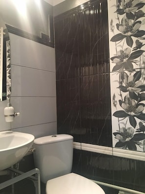 A bathroom with a white sink, toilet, and dark tiled walls. - Old Cracow Apartments (Kraków)