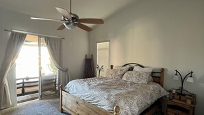 A bedroom with a wooden bed, a ceiling fan, a nightstand with a lamp, and a view of the outdoors through a sliding door.