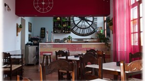 Un restaurante con sillas y mesas de madera, un reloj de pared grande y una zona de bar con estantes llenos de botellas.