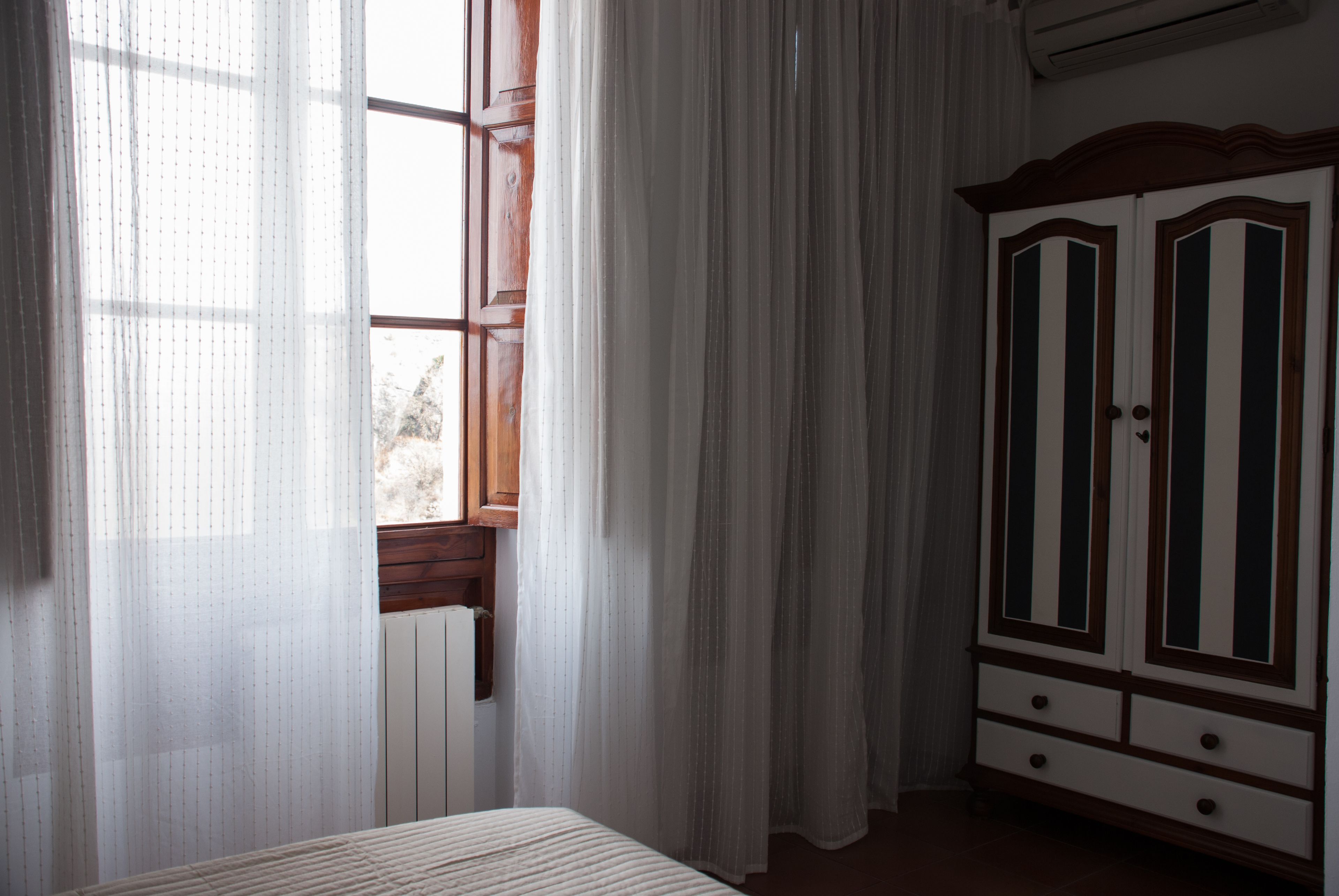 Una habitación con cama, ventana con cortinas y armario.