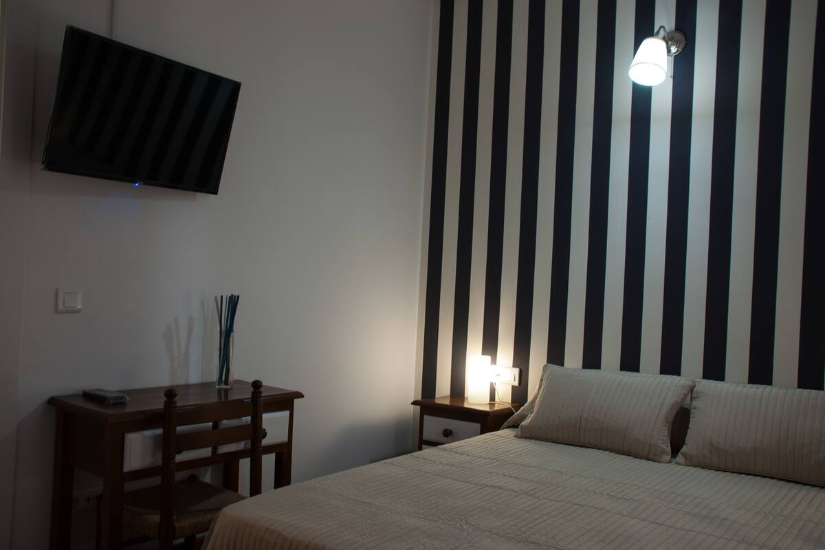 Une chambre à coucher comprenant un lit, un bureau, une chaise, un téléviseur fixé au mur et un mur à rayures.